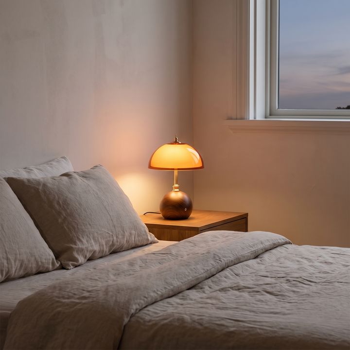 Cleo walnut and amber dome table lamp glowing on a bedside table