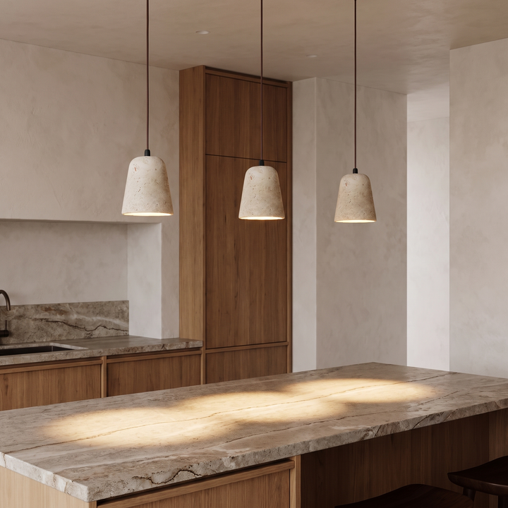 Three Signe travertine bell pendants lit above a kitchen island