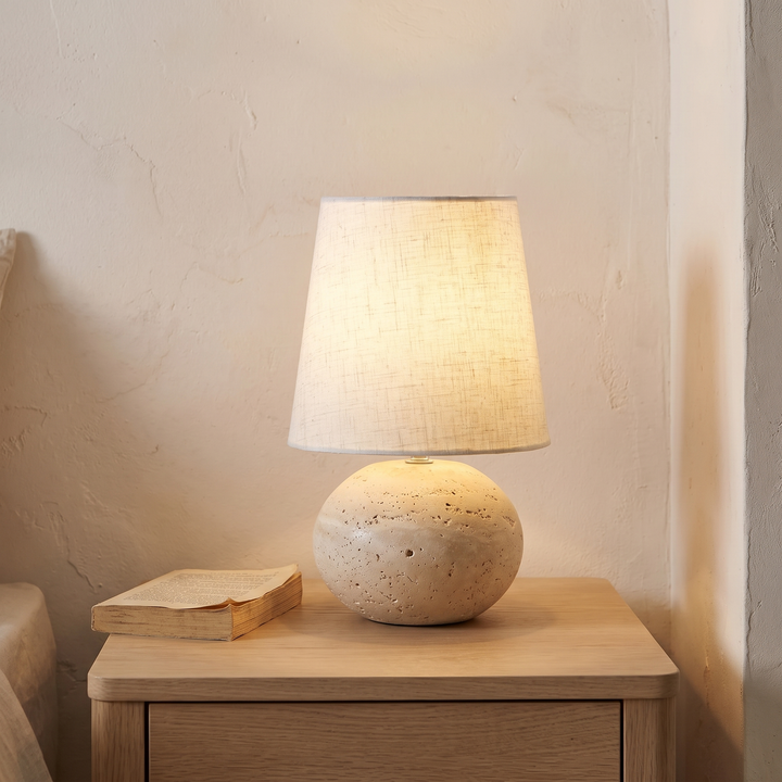 Nella travertine ball lamp with a linen shade on a bedside table