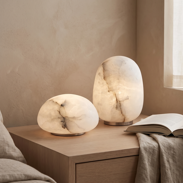 Two Tove alabaster lamps lit together on an oak bedside table