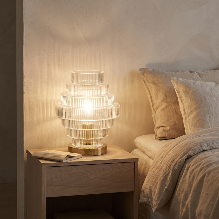 Lova ribbed glass table lamp lit on an oak bedside table