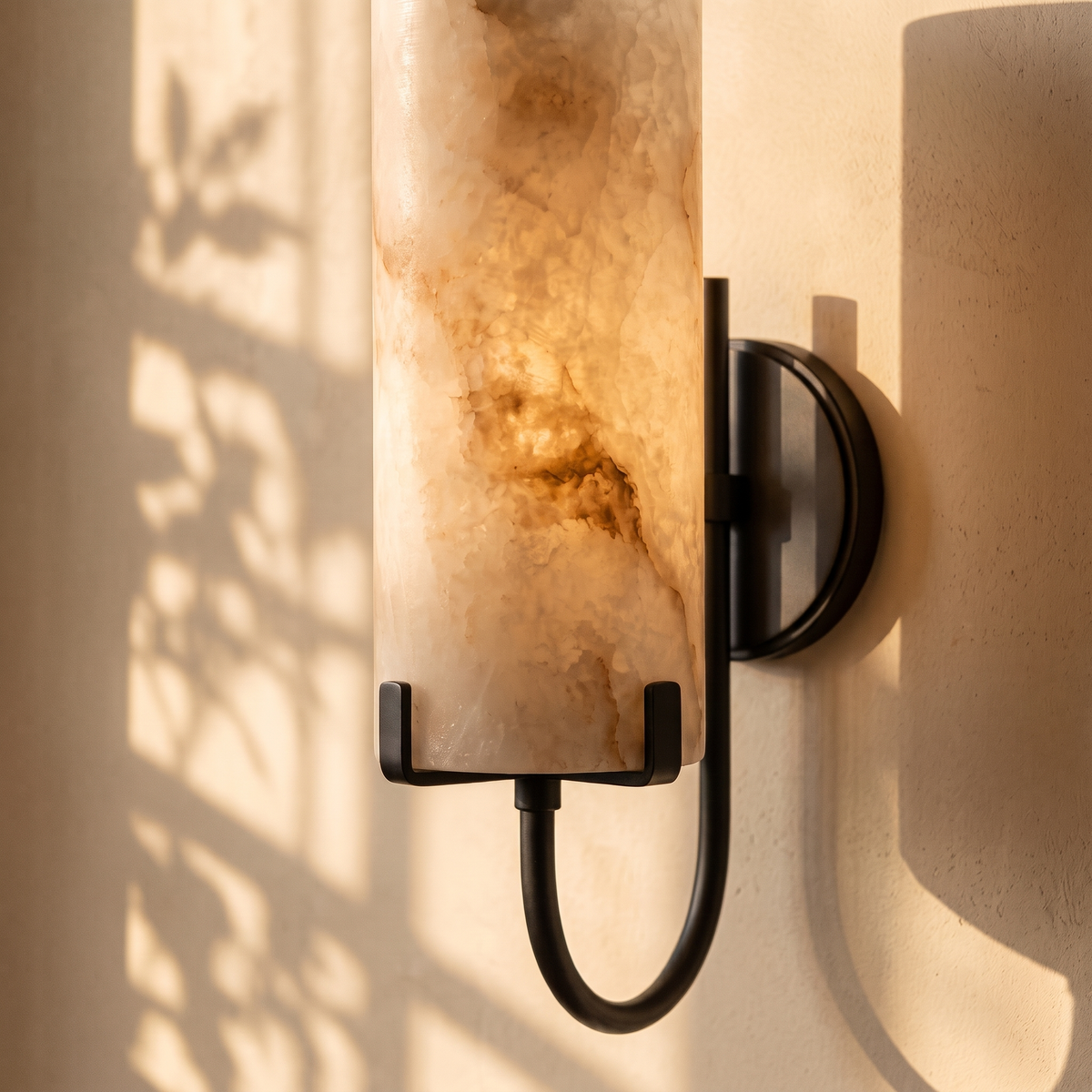 Tessara Loop curved arm marble wall sconce in matte black, lit on a plaster wall