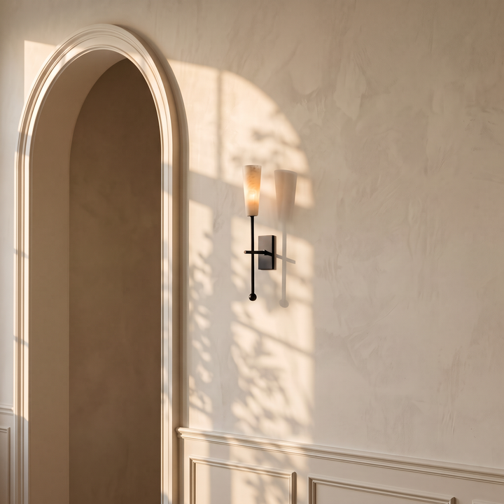 Tessara Torch tall marble wall sconce in matte black, lit on a warm plaster wall