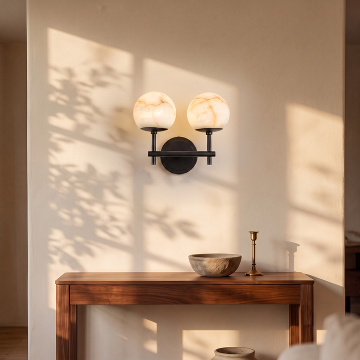 Orbella Twin double marble sphere wall sconce in matte black, lit above a console table