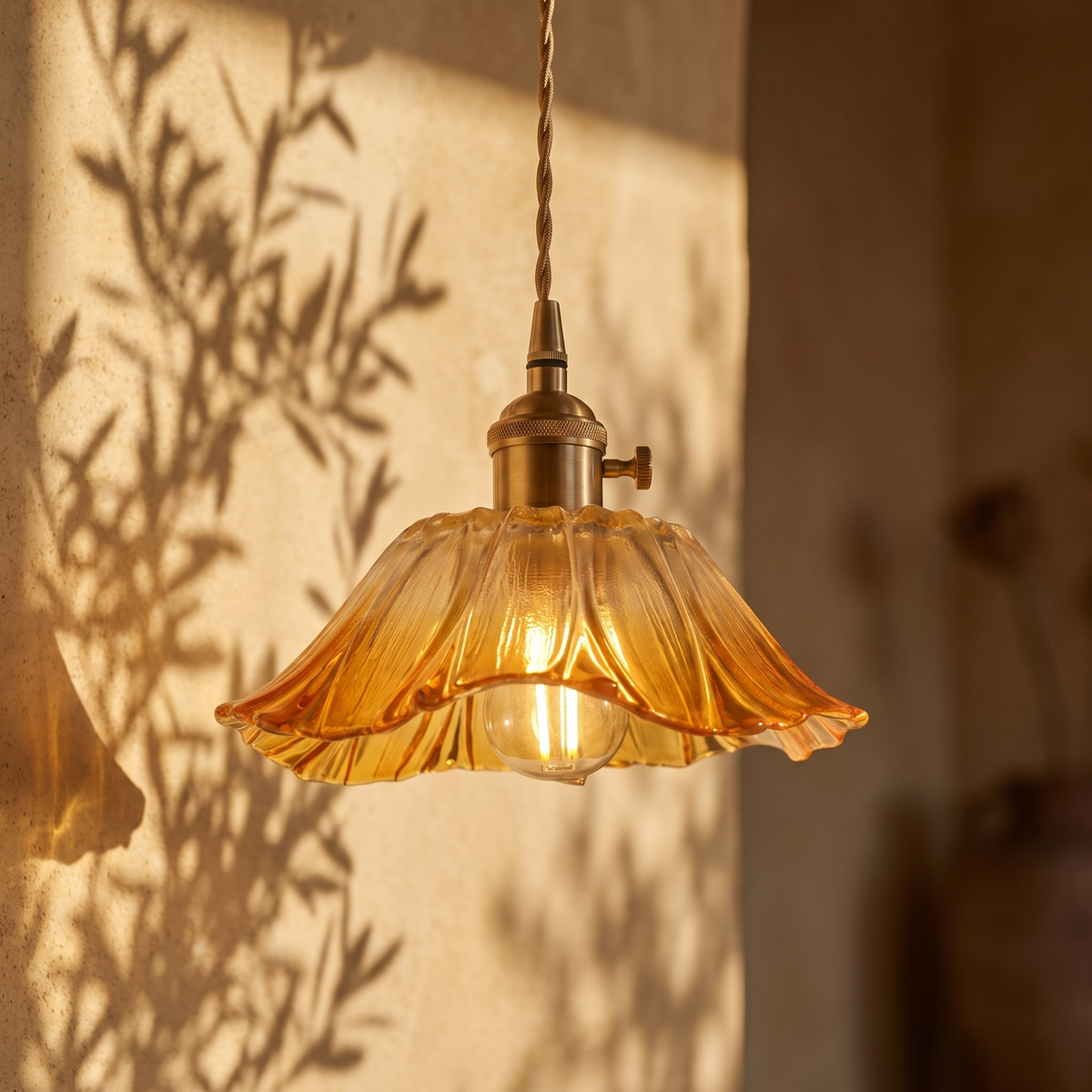 Fiorella petal glass cord pendant light in honey amber, lit against a plaster wall