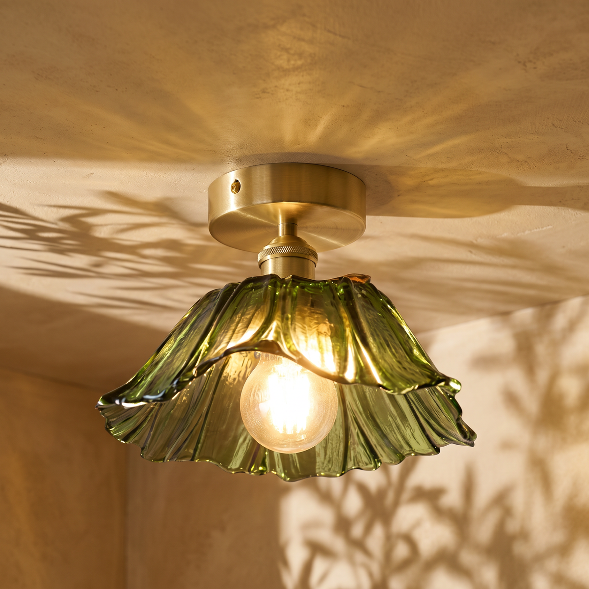 Fiorella flush mount petal glass ceiling light in leaf green, lit on a plaster ceiling