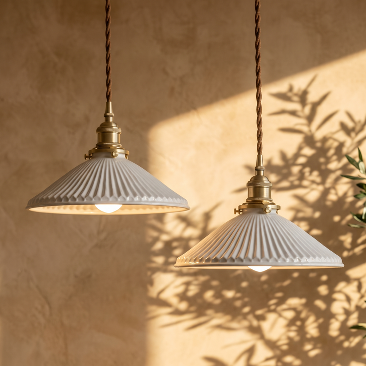 Two Bellora fluted ceramic brass pendant lights hanging side by side, lit against a plaster wall