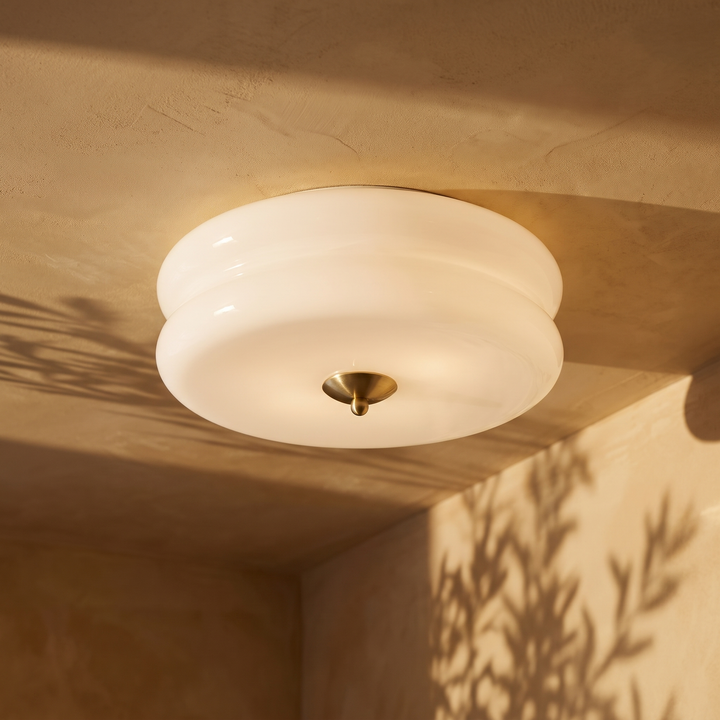 Deliona opal glass flush mount ceiling light in gold and white, lit on a plaster ceiling