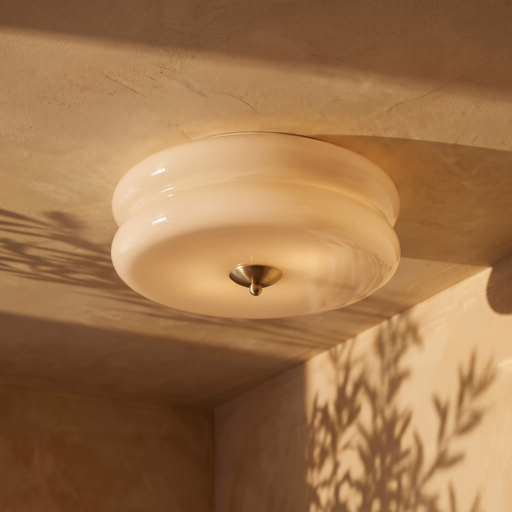 Deliona opal glass flush mount ceiling light in gold and beige, lit on a plaster ceiling
