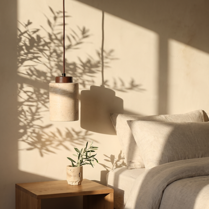 Edda Cylinder walnut travertine pendant light beside a linen dressed bed